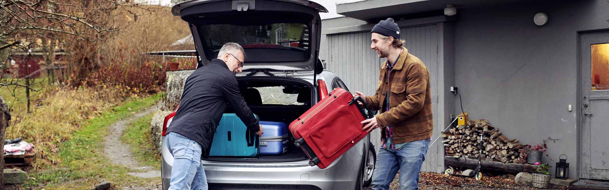 Två män packar in resväskor i bagageluckan på en bil